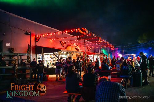 Guests gather beneath orange lights in the Fright Kingdom midway.